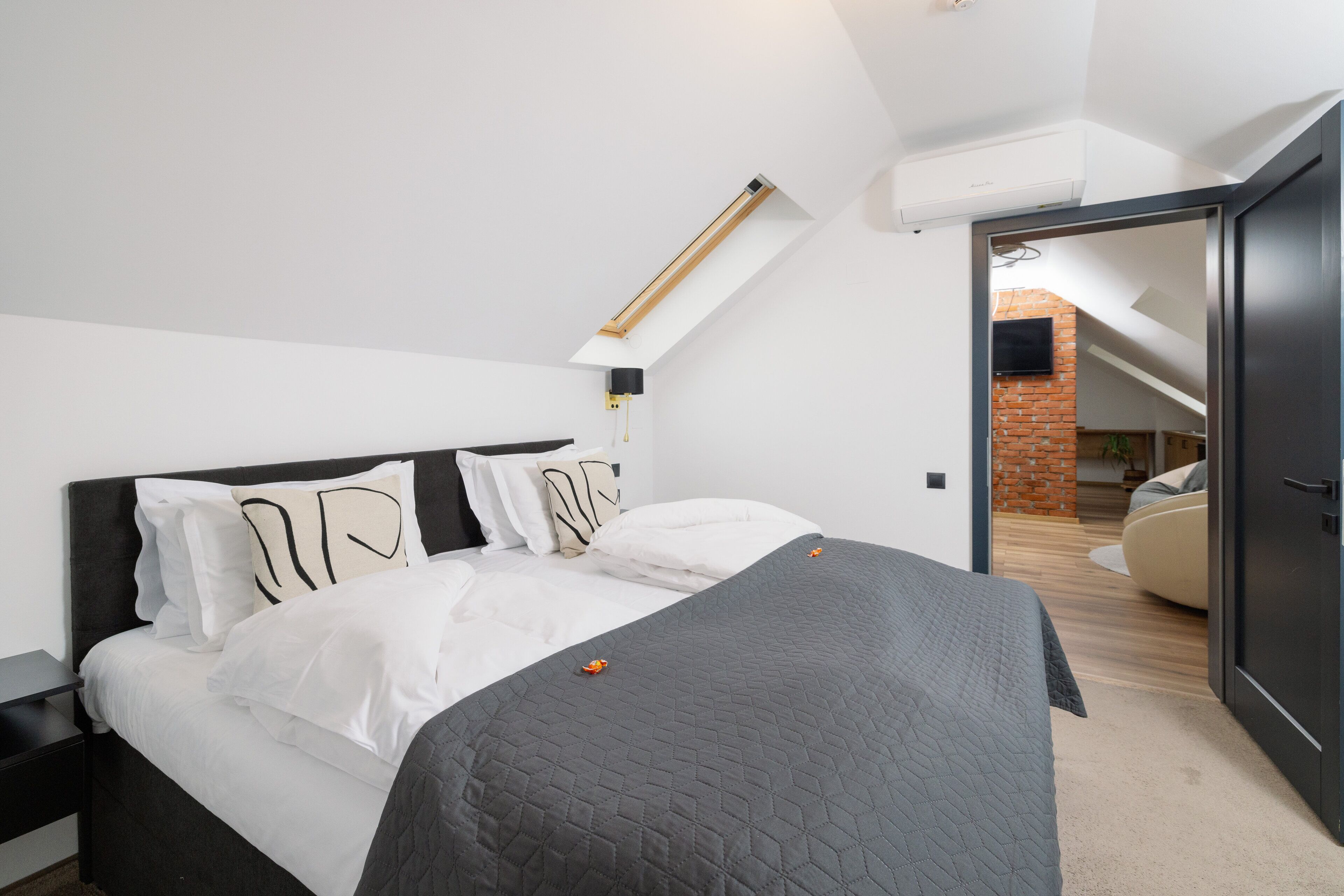 A modern bedroom with a bed, white bedding, a dark headboard, and a skylight.