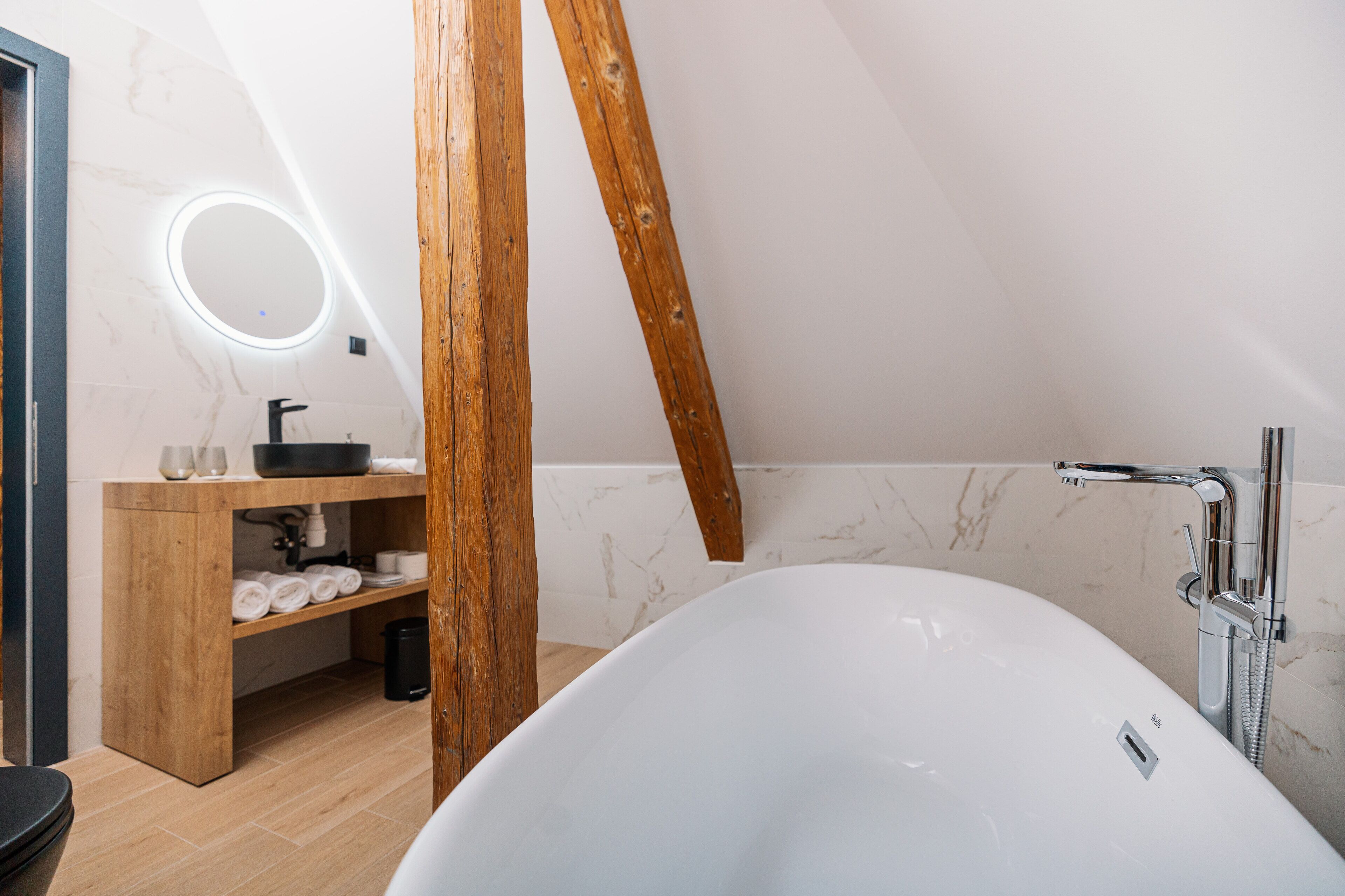 Un baño moderno con una bañera independiente, tocador de madera y un espejo circular.