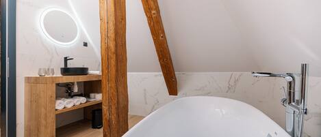 Un baño moderno con una bañera independiente, tocador de madera y un espejo circular.