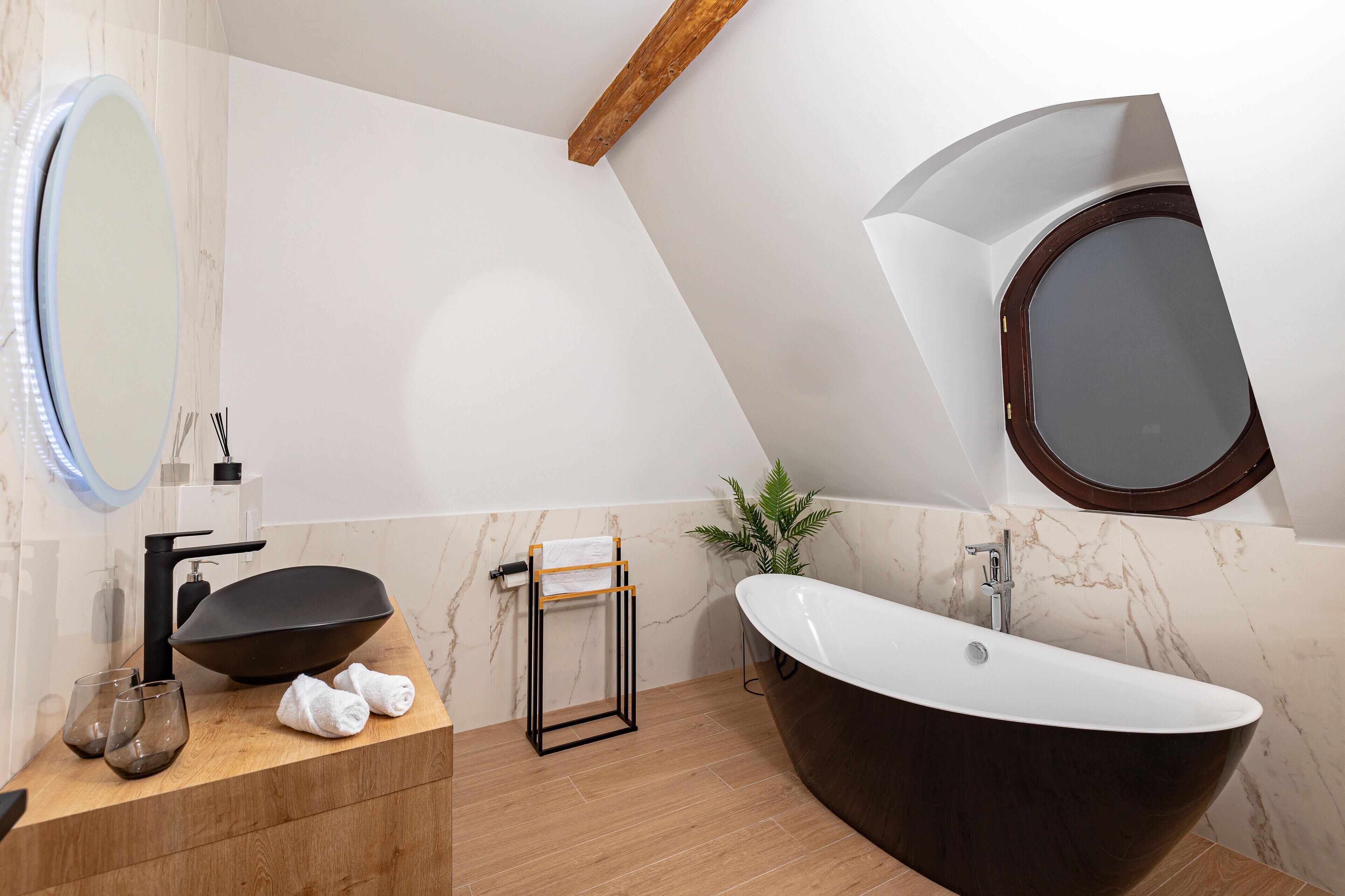 A modern bathroom with a freestanding bathtub, a round mirror, and a wooden vanity.