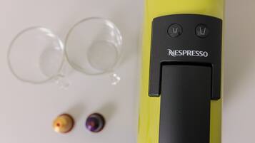 Une machine à café Nespresso jaune, avec deux capsules de café vides et deux tasses à café vides.
