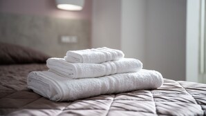 Un montón de toallas blancas dobladas impecablemente sobre una cama con cubierta texturizada.