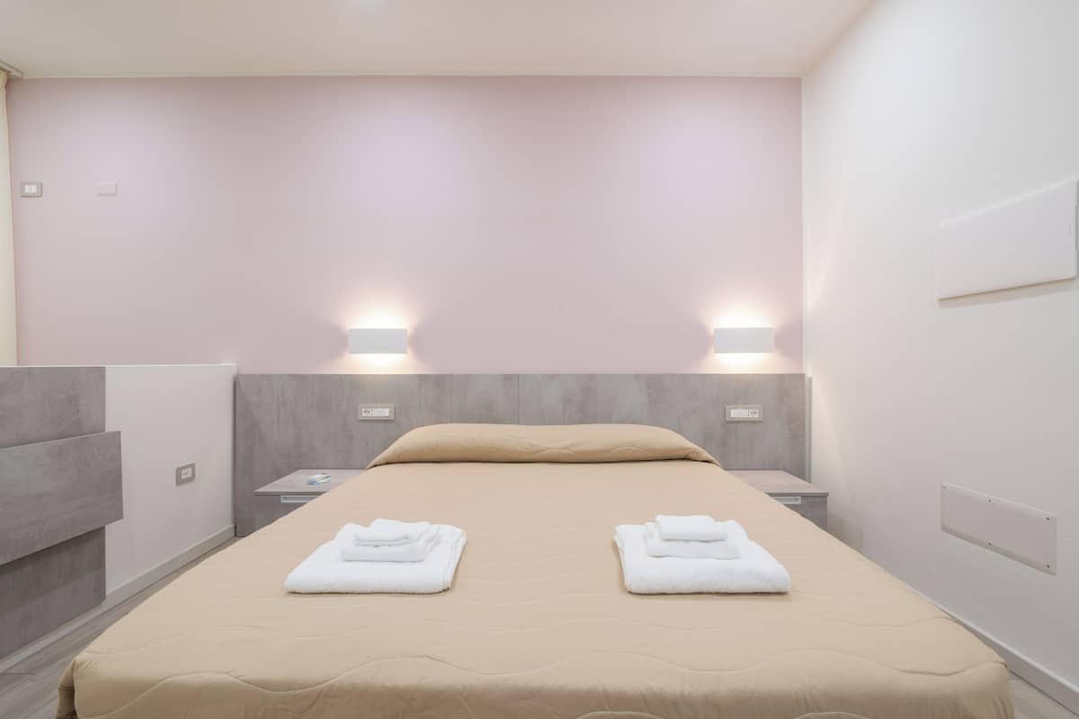 Habitación de hotel con cama, dos mesitas de noche, una lámpara de pared y un panel en la pared.