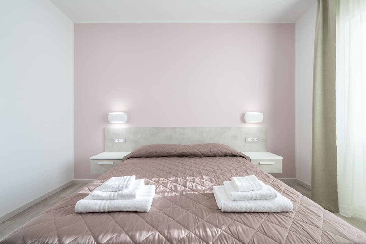Una cama bien hecha con un edredón rosa y dos toallas blancas dobladas encima.