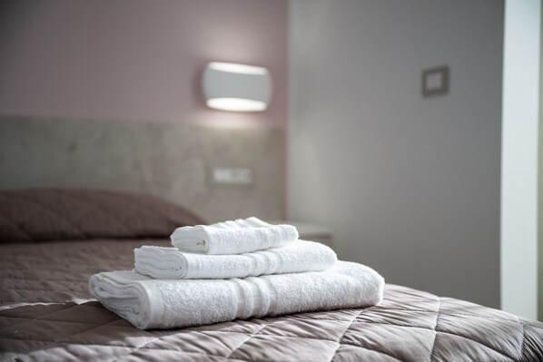 Una cama bien hecha con un edredón color beige y una pila de toallas blancas encima.