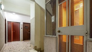 Un pasillo con suelo de baldosas, dos puertas de madera y una pared con ventanal de malla metálica.