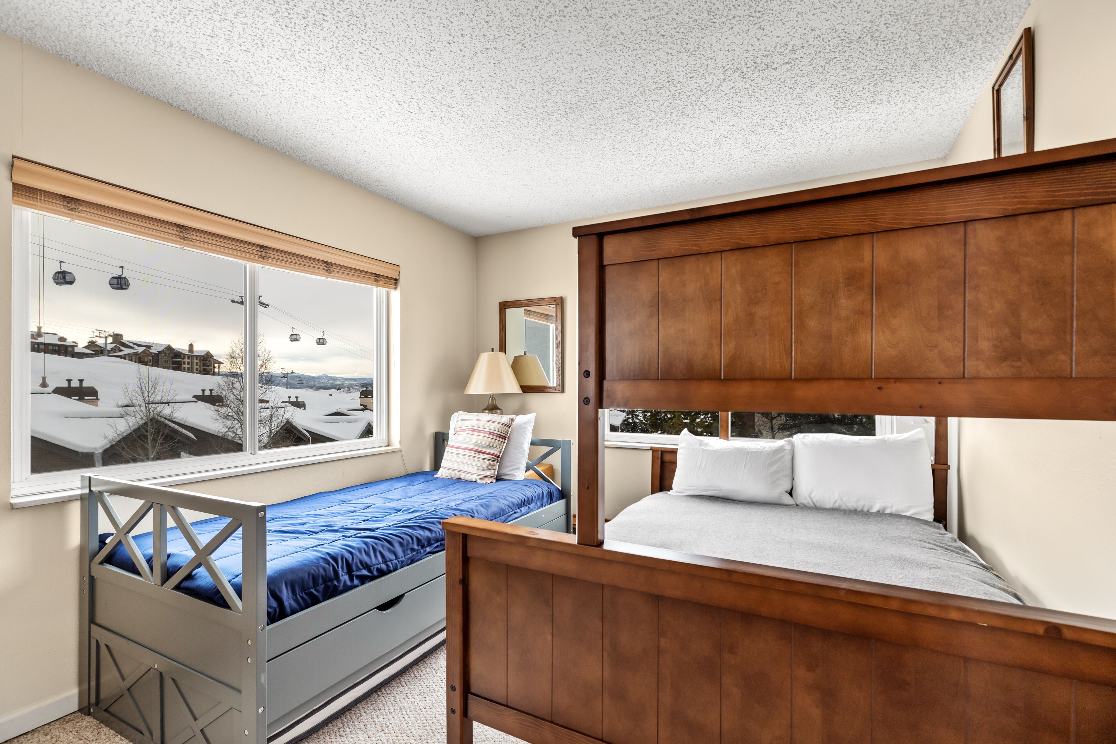 A bedroom with a bunk bed, a window with a view of a snowy landscape, and a bedside table with a lamp.