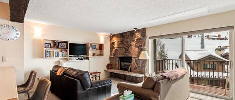 A living room with a fireplace, a sofa, a television, and a view of a snowy landscape through a large window.