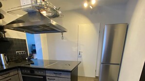 Eine Küche mit Edelstahl-Dunstabzugshaube, einem Backofen mit Platz für zwei Auflaufformen, einem Kühlschrank und Fliesenboden.