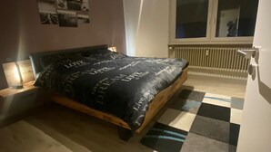 Ein Schlafzimmer mit einem Bett, einem Nachttisch, einem Fenster und einer Heizung.