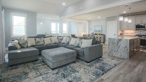 A spacious living room with a sectional sofa, ottoman, and a large rug.