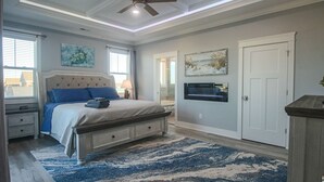 A bedroom with a bed, nightstands, a ceiling fan, a TV, and artwork on the walls.