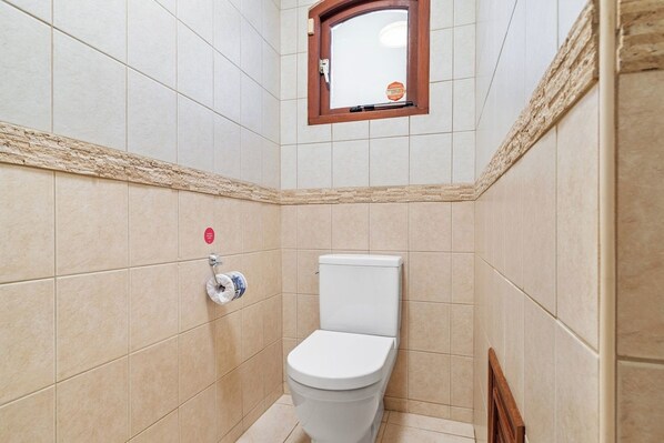 A small bathroom with a toilet, a towel dispenser, and a window.