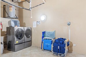 A laundry room with stacked washers and dryers, a blue folding cart, and a portable heater on the wall. - Serene 4BR Villa: Pool Views Oasis near Palm Beach (Noord)
