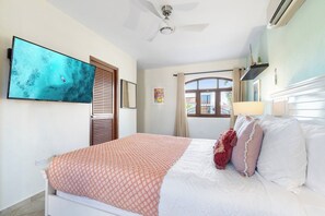 A bedroom with a bed, a ceiling fan, a TV, and a window with curtains.