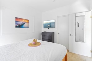 A bedroom with a bed, a wall-mounted TV, a door, and a painting.
