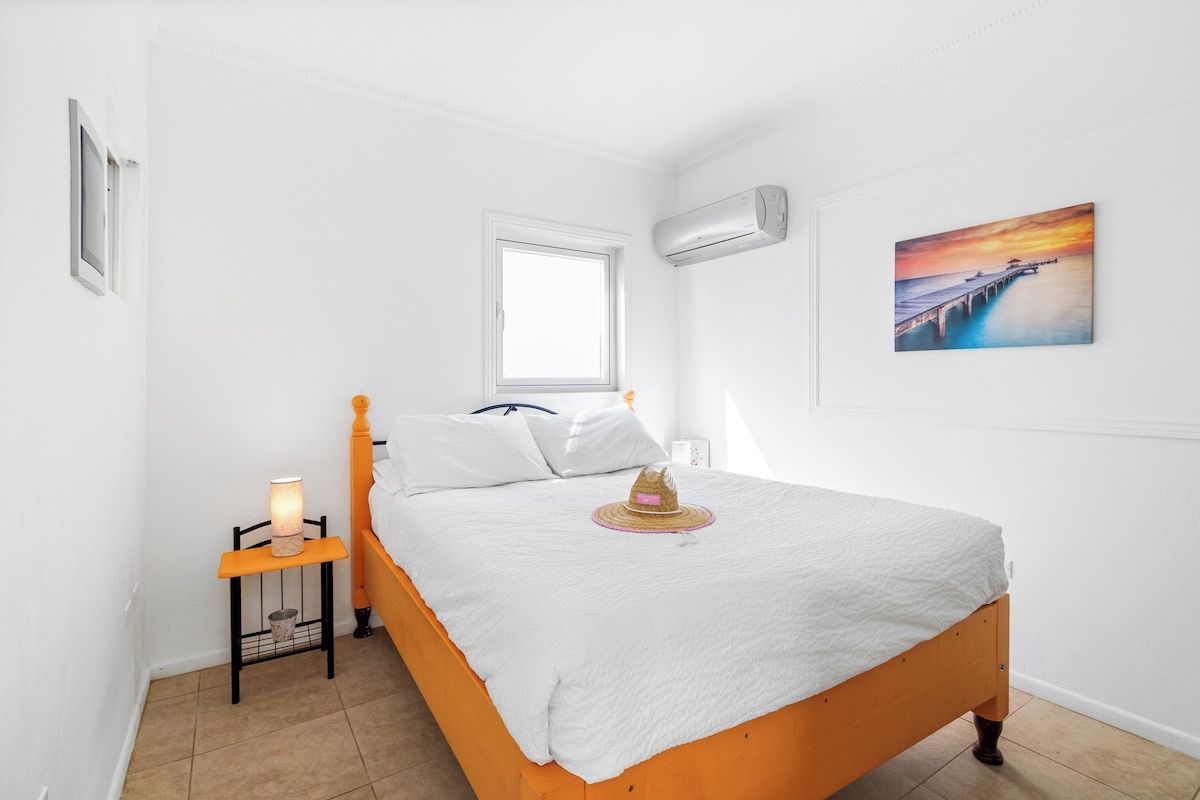 Une chambre à coucher avec un lit, une table de chevet, une lampe, une fenêtre et un tableau au mur.