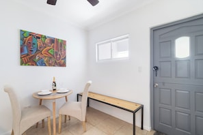 A room with a dining table, chairs, a bench, a door, a window, and a colorful abstract painting on the wall.