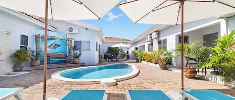 A pool area with lounge chairs, umbrellas, and a mural on the wall.