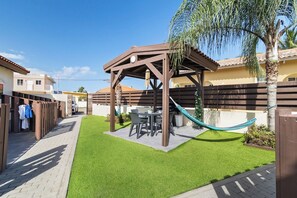 Un espace patio agrémenté d’une pergola en bois, d’un hamac et d’une table avec des chaises.