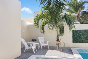 A poolside area with a white chair, a small table, and a palm tree.