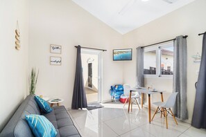 A modern living room with a sofa, a dining table with chairs, a small side table, and a view of the outside.