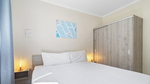 Een hotelkamer met een bed, een nachtkastje met een lamp, een kledingkast en een kunstwerk aan de muur.
