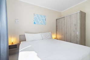 A hotel room with a bed, a nightstand with a lamp, a wardrobe, and a wall-mounted artwork. - Captivating 1BR Home w/ Pool near Palm Beach (Noord)