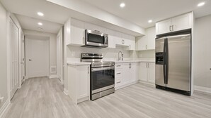 A modern kitchen with white cabinetry, stainless steel appliances, and a light wood floor.