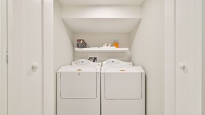 A laundry room with two white dryers and a shelf above them.