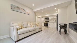 A modern living room with a beige sofa, a dining table, and a kitchen in the background.
