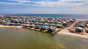 An aerial view of a coastal residential area with houses on stilts over water, a beach, and the ocean in the background. - Bayfront, amazing views, waterside decking, close to everything! – Sunscape (Dauphin Island)