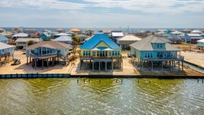 A coastal residential area with houses on stilts over water, featuring a clear view of the ocean and a sandy beach. - Bayfront, amazing views, waterside decking, close to everything! – Sunscape (Dauphin Island)