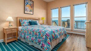 A bedroom with a bed, a nightstand, a lamp, and a window with a view of the ocean. - Bayfront, amazing views, waterside decking, close to everything! – Sunscape (Dauphin Island)