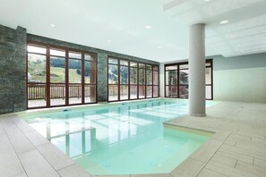En stor inomhuspool med väggar av genomskinligt glas och en bakgrund av stenmur.