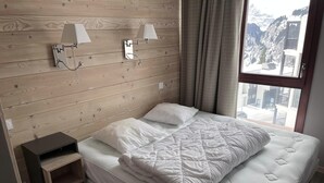 Una camera da letto con una testiera in legno, due abat-jour, un letto con coperta trapuntata, un comodino e una finestra con vista sulle montagne.