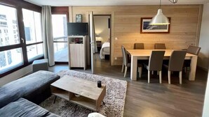 Un soggiorno moderno con divano, tavolino e zona pranzo con sedie e tavolo. Si nota una TV e un piccolo mobile sullo sfondo.