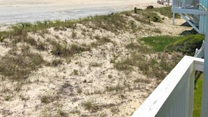 A beach view from a balcony with a clear sky, sandy beach, and a building with a balcony. - Peach on the Beach Oceanfront  (Kure Beach)
