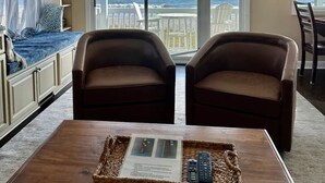 A living room with a view of the ocean, a ceiling fan, and a dining area with chairs. - Peach on the Beach Oceanfront  (Kure Beach)