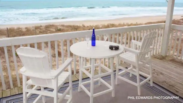 A white outdoor seating area with a table and chairs, overlooking a beach with waves. - Peach on the Beach Oceanfront  (Kure Beach)