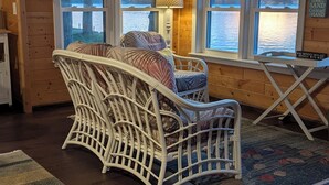 L’intérieur d’un chalet accueillant, avec un fauteuil en osier, une petite table et une vue sur un lac par de grandes fenêtres.