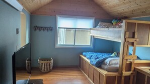 Une pièce avec un plafond en pente, un plancher en bois, des lits superposés, une fenêtre et un ventilateur de plafond.