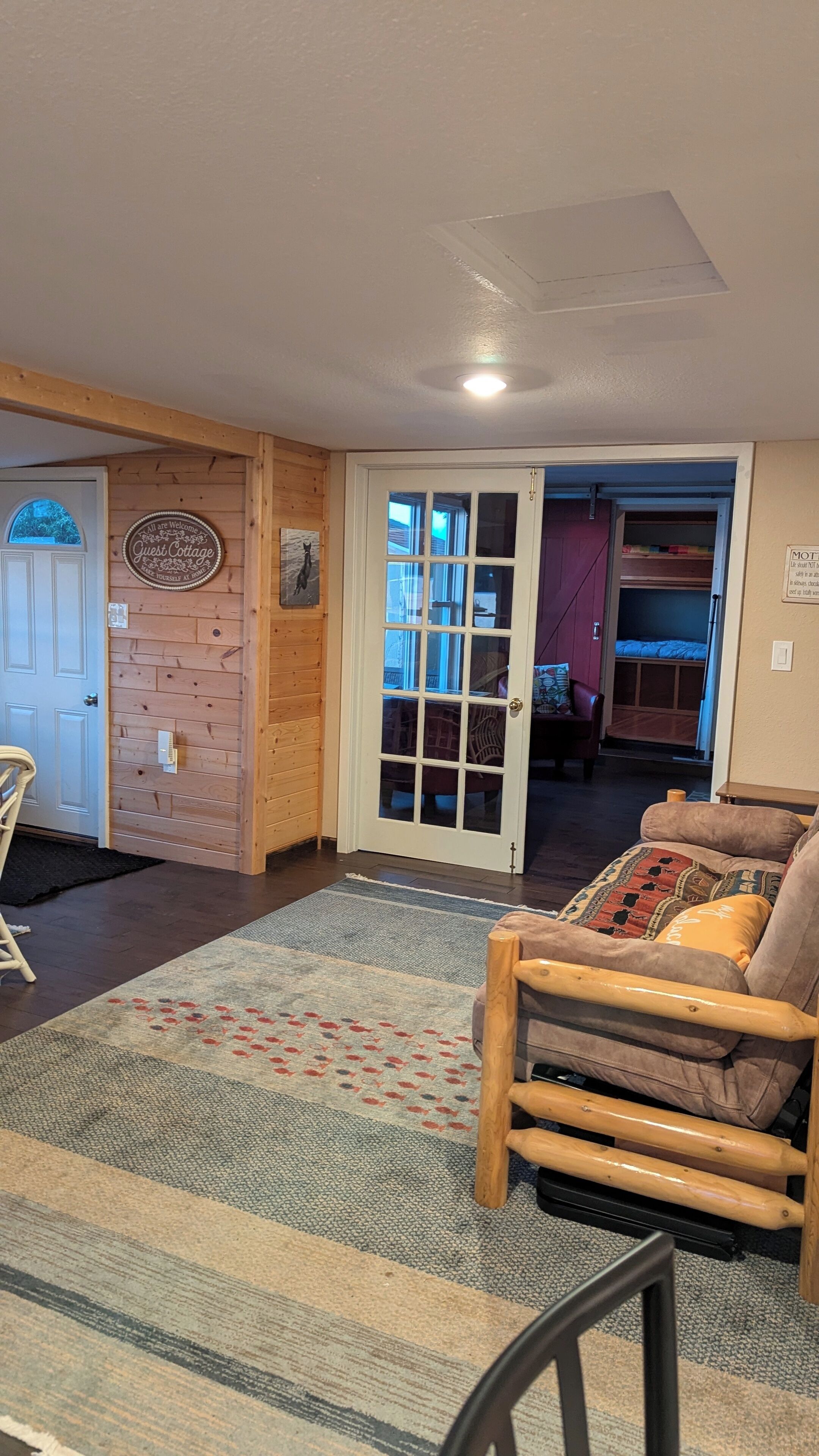 A cozy room with a wooden wall, a white door, and a view of a bunk bed through a glass door.
