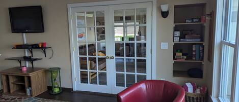 A living room with a television, a bookshelf, a red leather chair, and a door with glass panels.