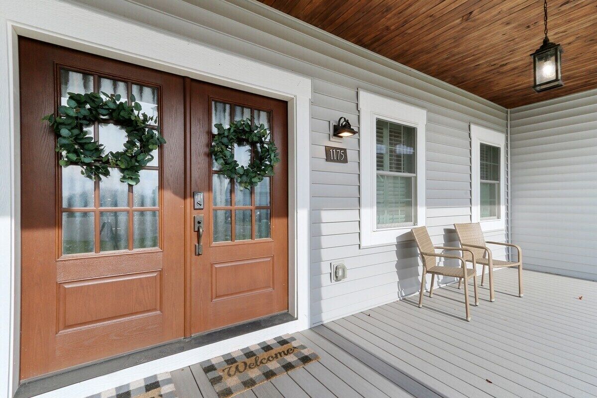 A front porch with two wooden doors, a welcome mat, and two wicker chairs.