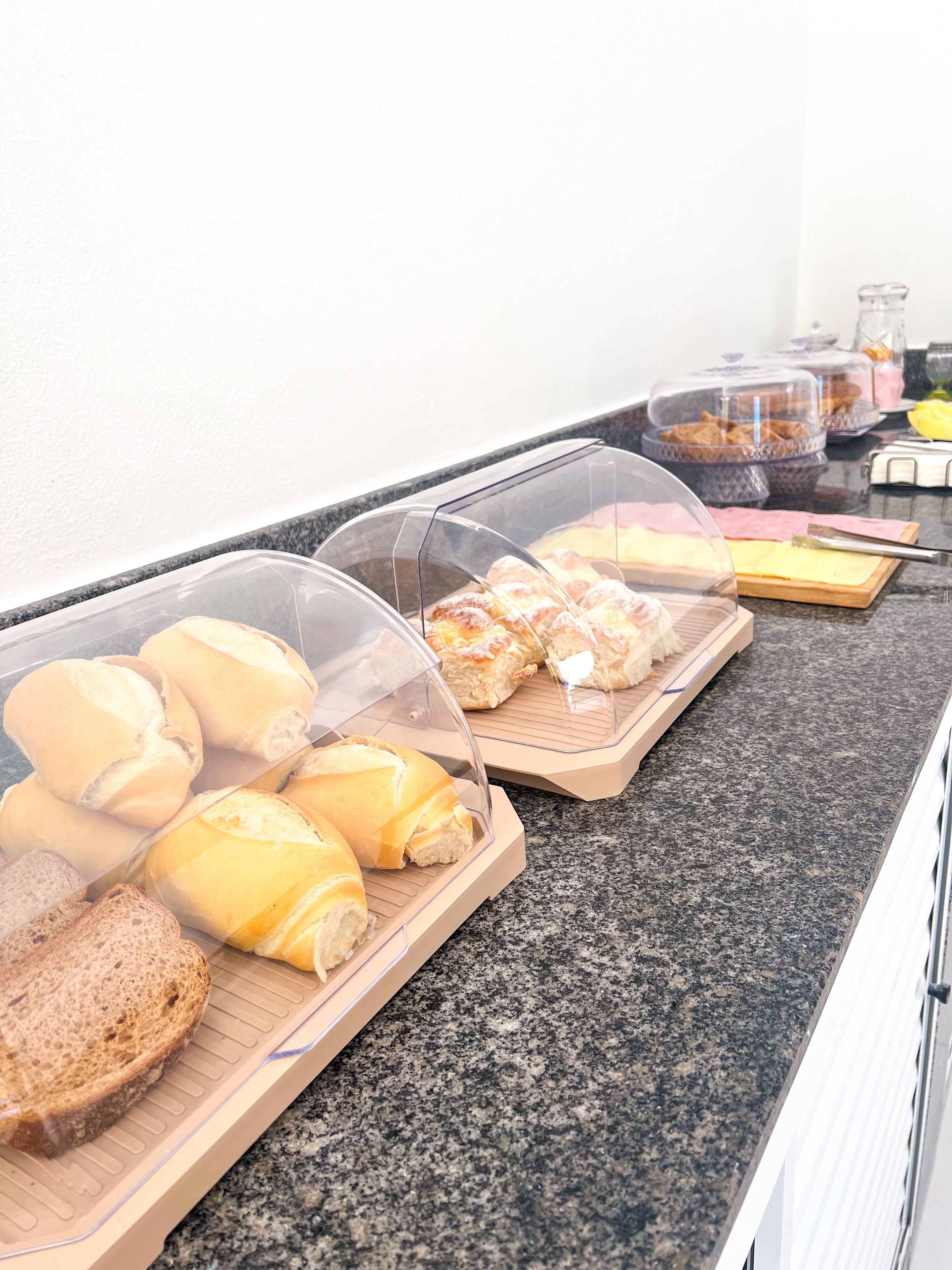 A breakfast buffet with various breads and pastries under clear plastic covers.