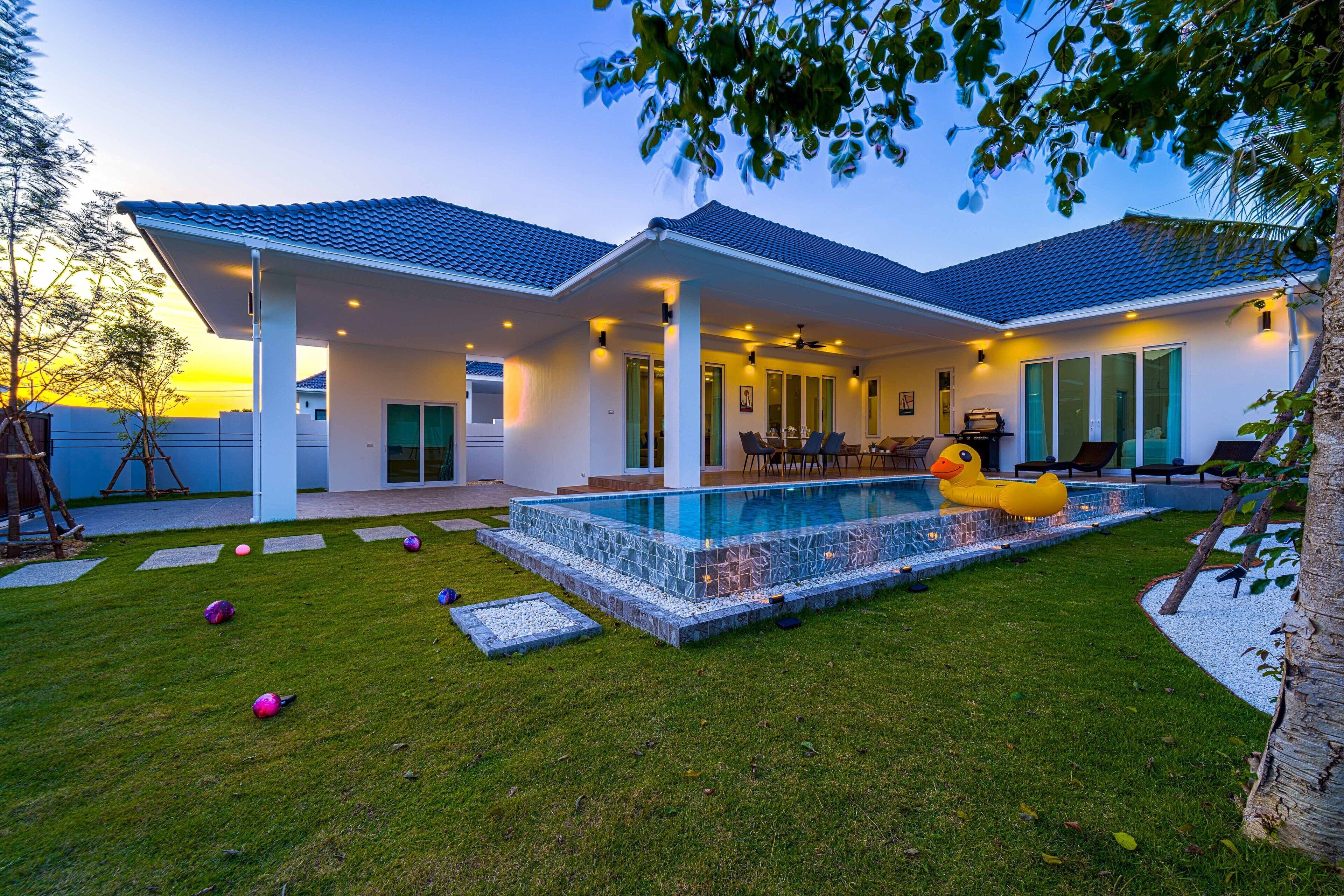 A modern house with a swimming pool, covered patio, and a well-maintained lawn.