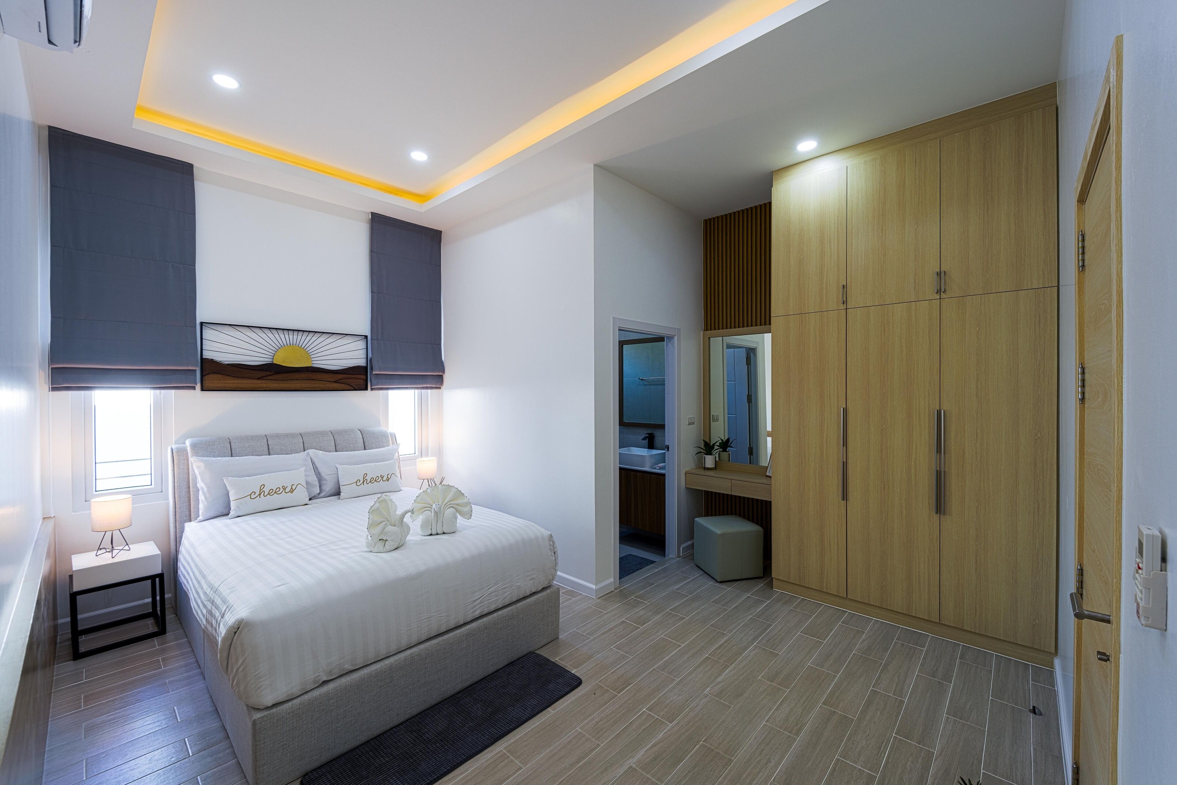 A modern bedroom with a large bed, bedside lamps, a nightstand, a wardrobe, and a bathroom visible through an open door.