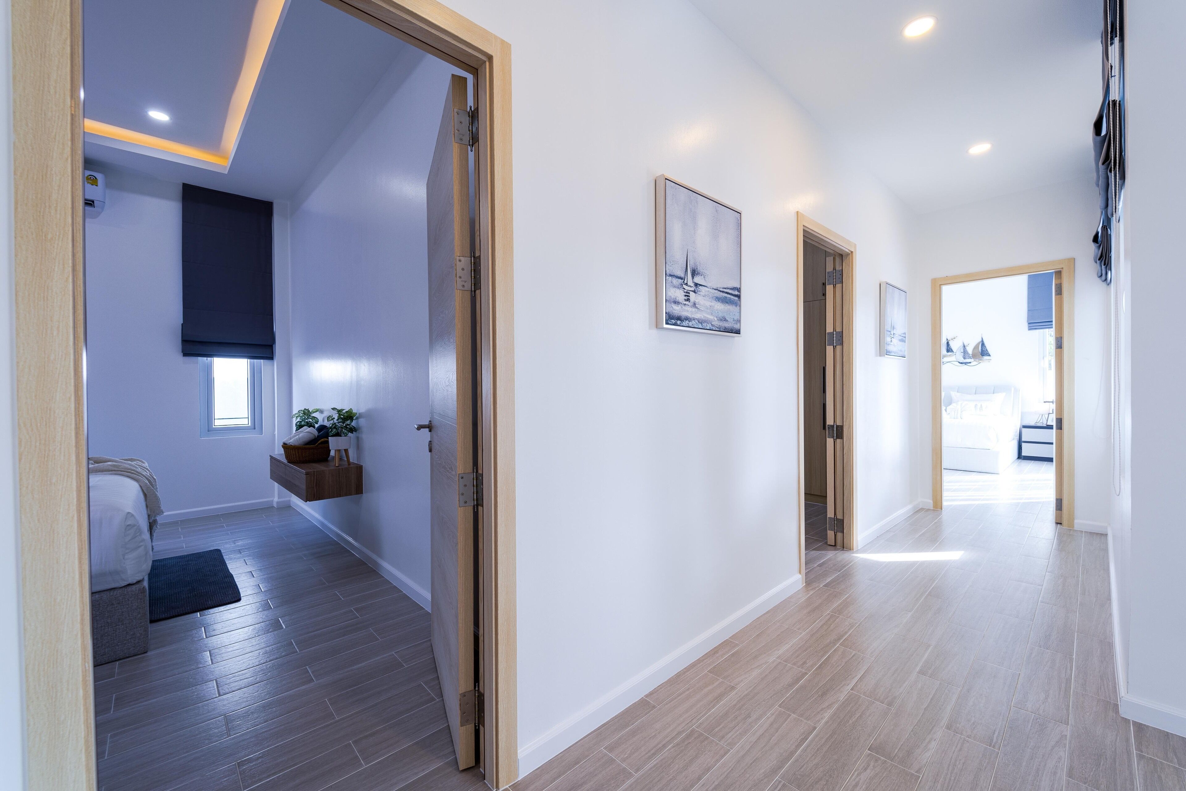 A modern hallway with wooden flooring, a bed with a dark-colored rug, and a small plant on a shelf.