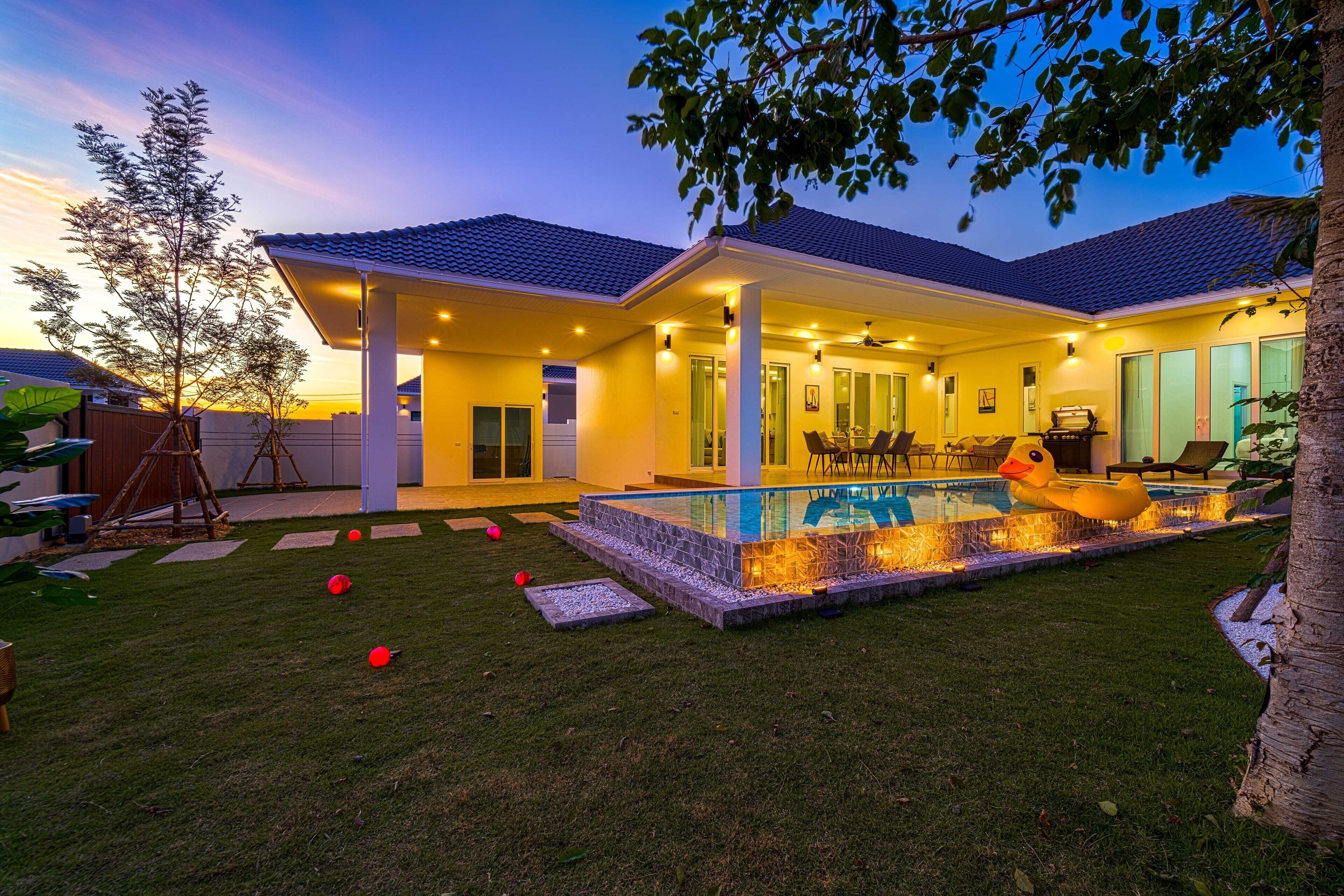 A modern house with a swimming pool, covered patio, and a well-maintained lawn.